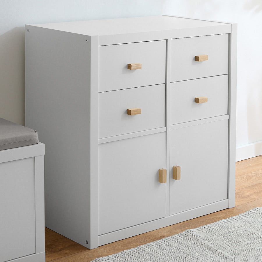 Ein weißes IKEA Kallax mit insgesamt 4 Fächern, welche mit Türen und Schubladen gefüllt wurden. An den Fronten sind eckige Holzgriffe aus Eiche zu sehen.