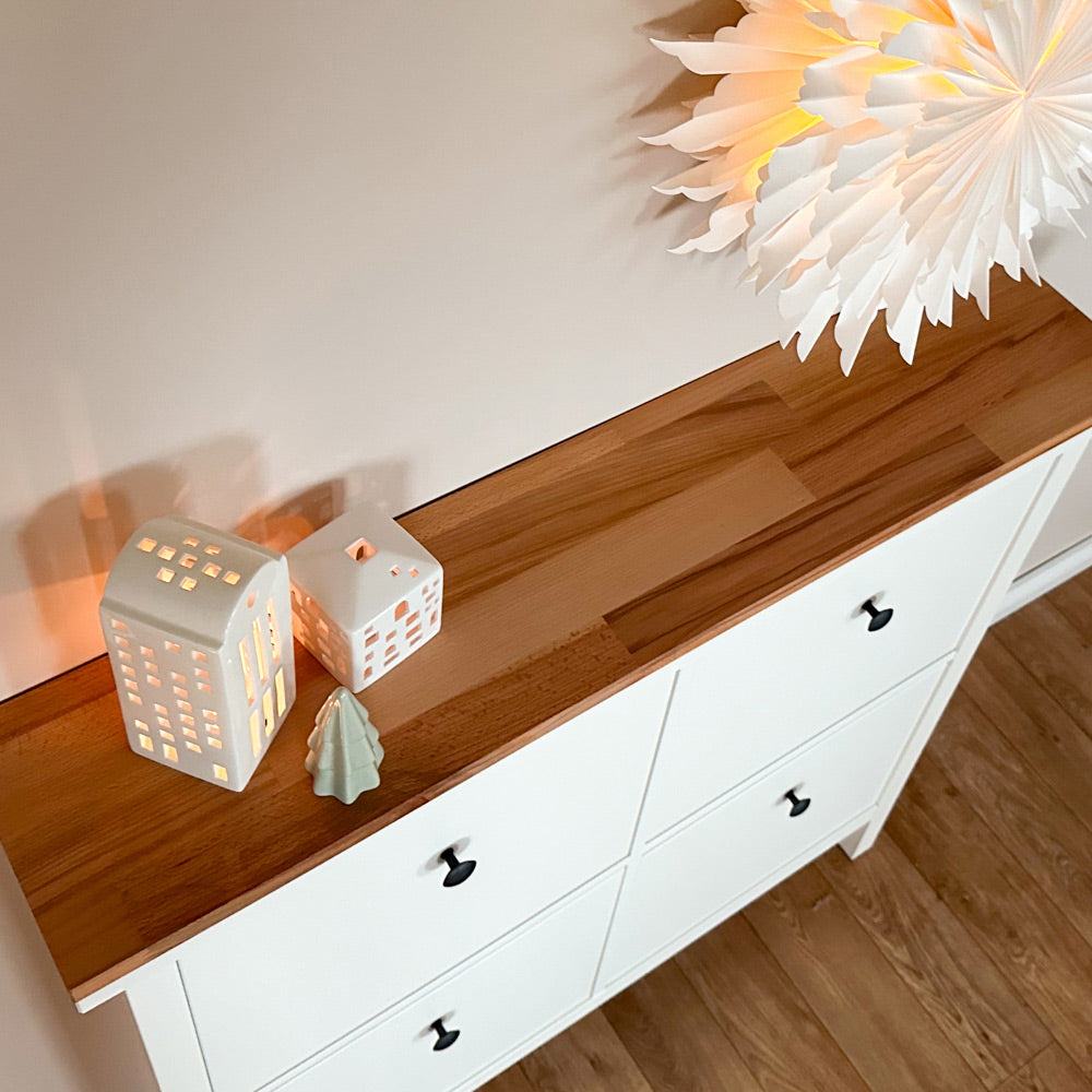 Sicht von oben auf eine Buchenholzplatte, die auf einem weißen IKEA Hemnes Schuschrank 4 Fach liegt. Auf der Platte sind noch Windlichter zu sehen.