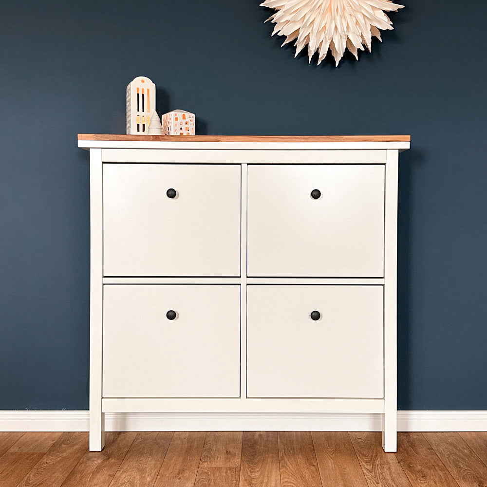 Frontalansicht von einem weißen IKEA Hemnes Schuschrank mit 4 fächern vor einer blauen Wand. Auf dem Schuhschrank liegt eine Massivholzplatte aus Buche.