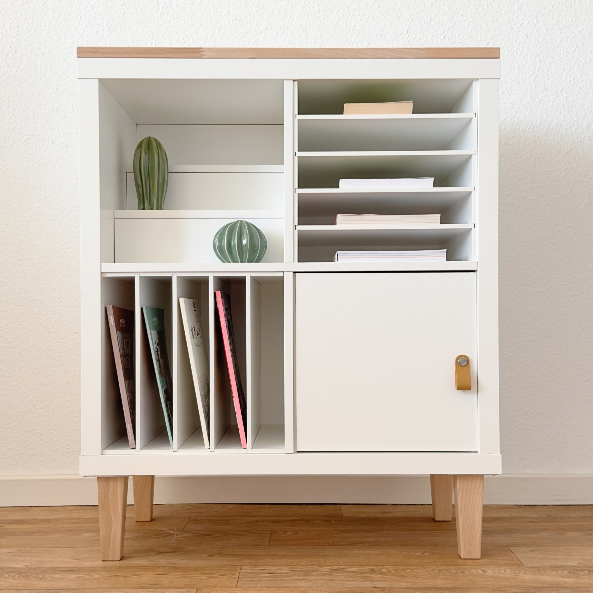 Weißes IKEA Kallax Regal mit Holzplatte, Holzfüßen und verschiedenen Einsätzen.