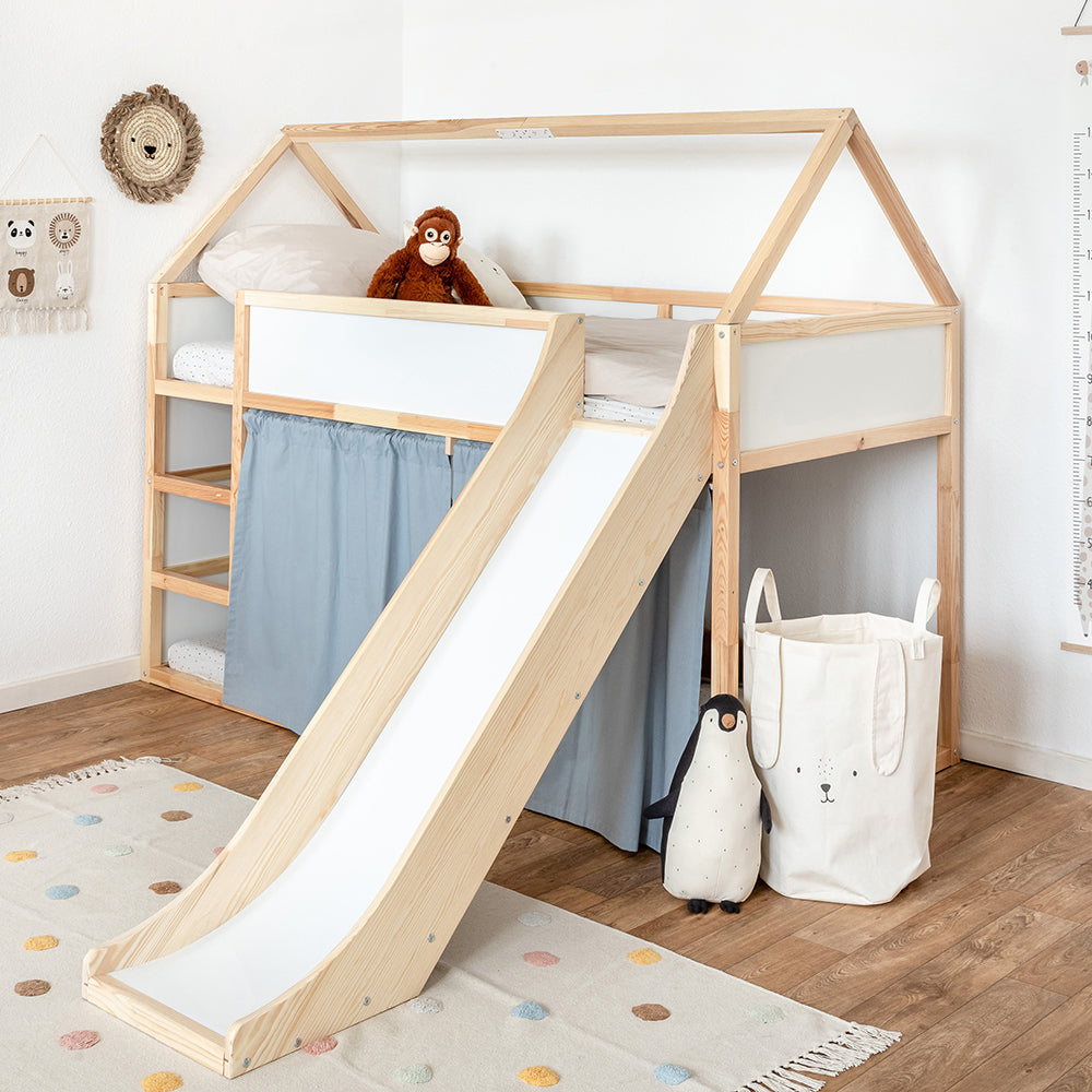 Kura Bett von Ikea als Hochbett im dekorierten Kinderzimmer mit blauen Vorhängen, einem Dachgestell aus Holz und einer passgenauen Rutsche. Durch das Zubehör wirkt das Kura Bett wie ein Hausbett und die Kinder können sich in der unteren Ebene hinter den Vorhängen verstecken.