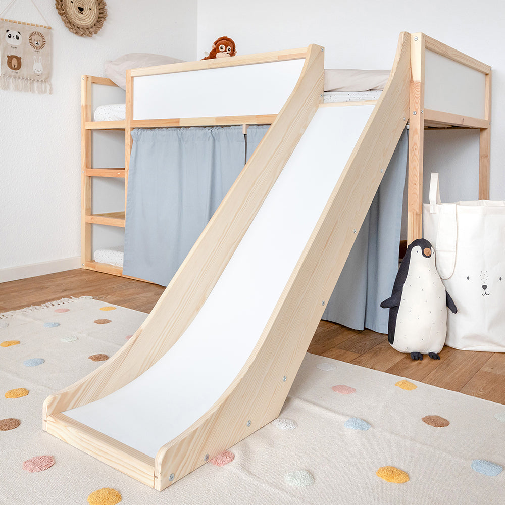 Kinderzimmer mit einem Kura Bett und passgenauer Kura Rutsche. Das Zimmer ist schlicht dekoriert und das Kura Bett zusätzlich mit blauen Vorhängen ausgestattet.