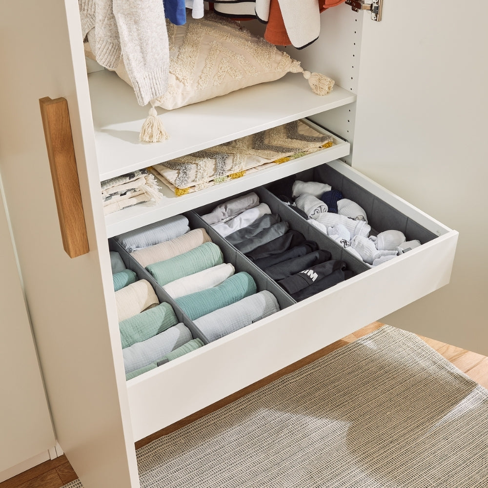 Eine offene, 100 cm breite Schublade im IKEA Pax Kleiderschrank. In der Schublade sind 4 gleich große Schubladen Organizer, die mit Kleidung gefüllt sind.