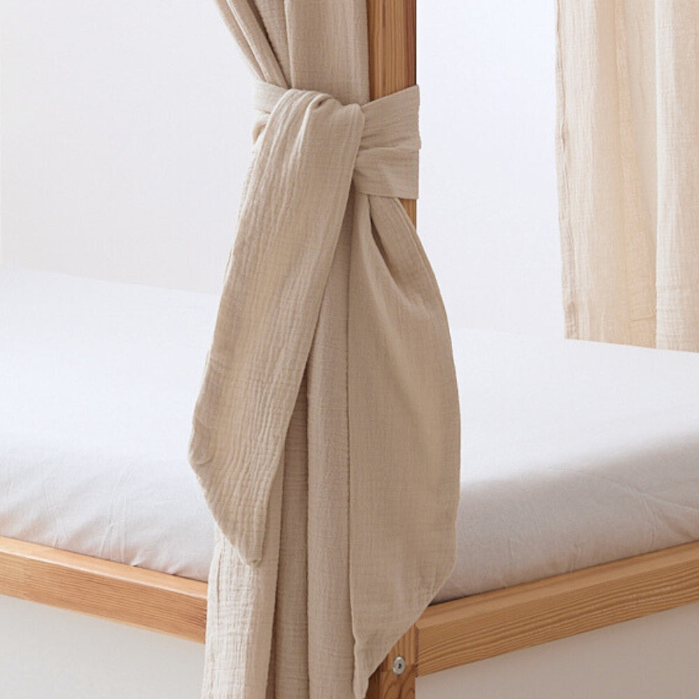 Kura Baldachin aus Musselin in Beige ist mit einem Band am Bettpfosten befestigt.