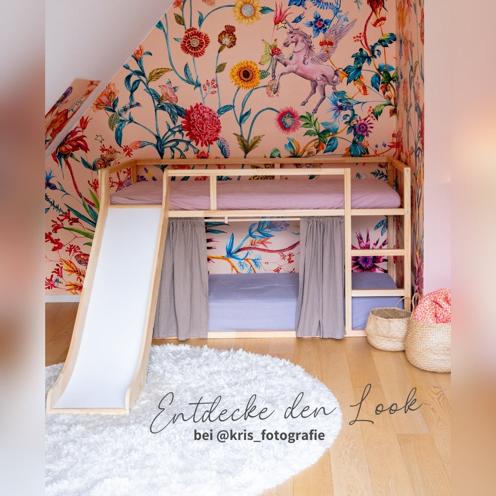 Inspiration der Rutsche fürs Kura Bett im Kinderzimmer der Influencerin @kris_fotografie. Das Kura Bett steht an einer Wand mit einer bunten, floralen Tapete mit Einhörnern. Unter der Rutsche fürs Hochbett befindet sich ein runder weißer Teppich.